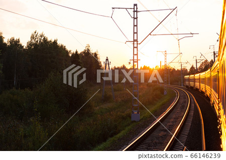An electric locomotive. The train takes me into the sunset. Railway tracks curve. 66146239