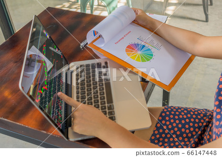 Woman pointing at financial candlestick graph on laptop at cafeteria 66147448