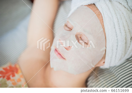 Young red-haired woman relaxing on a bed. Sheet mask on her face Young red-haired woman relaxing on a bed. Sheet mask on her face 66151699