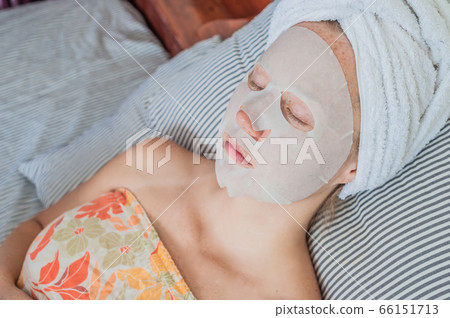 Young red-haired woman relaxing on a bed. Sheet mask on her face 66151713