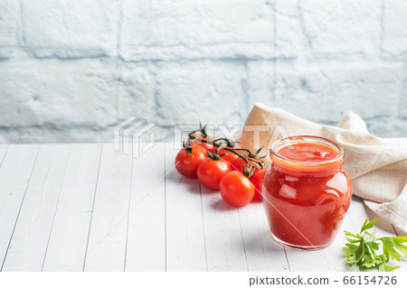 Tomatoes in their own juice or Tomato paste in a glass jar and fresh tomatoes on a white wooden table. Copy space 66154726