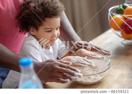 Cute little mulatta sitting at the table and getting ready to cook with her father 66159321