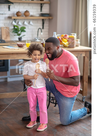Cute kid witin pink pants and her father holding spoons and singing a song 66159339