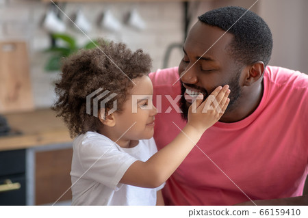 Sweet little girl touching her fathers face and looking pleased 66159410