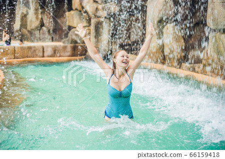 Young woman relaxing under a waterfall in aquapark Young woman relaxing under a waterfall in aquapark 66159418