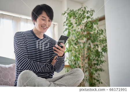 A young man looking at his smartphone at home A young man looking at his smartphone at home 66171991