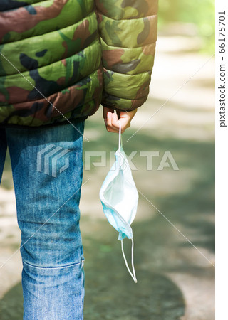 Protective face mask in a teenager's hand walking in the open fresh air in a park at the sunny day. Protective face mask in a teenager's hand walking in the open fresh air in a park at the sunny day. 66175701