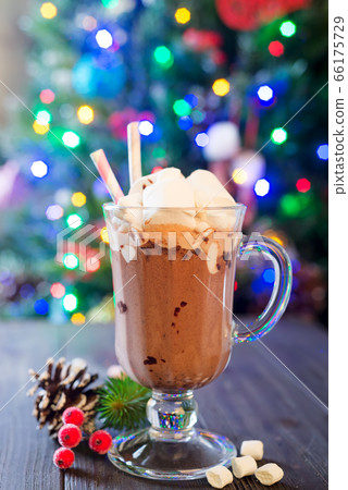 Glass cup of hot cocoa with mini marshmallows with pine boughs a rustic background with beautiful Christmas lights of bokeh. Could also be coffee. Glass cup of hot cocoa with mini marshmallows with pine boughs a rustic background with beautiful Christmas lights of bokeh. Could also be coffee. 66175729