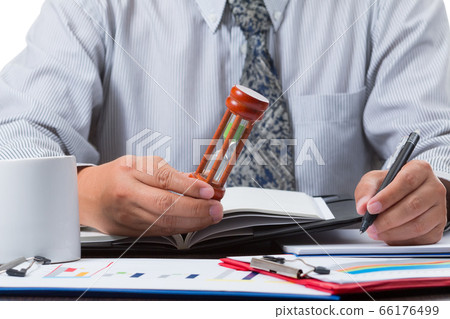 businessman taking note from the sale figure report and checking time from sandglass by close up businessman taking note from the sale figure report and checking time from sandglass by close up 66176499