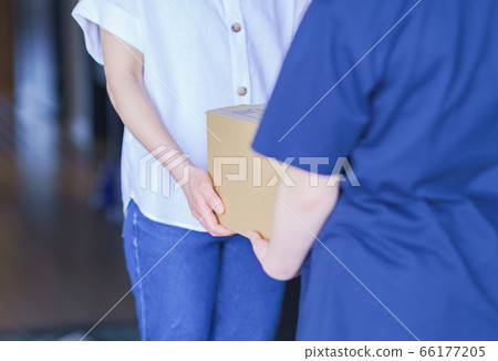 A delivery man delivering a parcel for online shopping and a housewife receiving it at the front door of the apartment 66177205