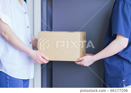 A delivery man delivering a parcel for online shopping and a housewife receiving it at the front door of the apartment A delivery man delivering a parcel for online shopping and a housewife receiving it at the front door of the apartment 66177206