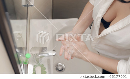 Beauty woman washes her hands with soap. Charming caucasian lady carefully soaping hands with soap suds while standing near the washbasin in bathroom. Sexuality and hygiene concept Beauty woman washes her hands with soap. Charming caucasian lady carefully soaping hands with soap suds while standing near the washbasin in bathroom. Sexuality and hygiene concept 66177991