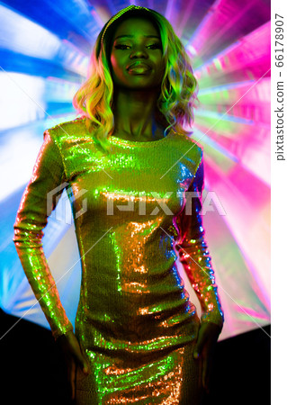 Sexy African woman in neon glow. Dark skinned lady in glittering dress poses looking at camera. Silhouette of stylish model in bright colors of neon lighting. Vogue concept Sexy African woman in neon glow. Dark skinned lady in glittering dress poses looking at camera. Silhouette of stylish model in bright colors of neon lighting. Vogue concept 66178907