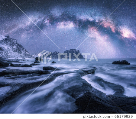 Milky Way over the snow covered mountains and rocky beach in winter at night in Lofoten Islands 66179929