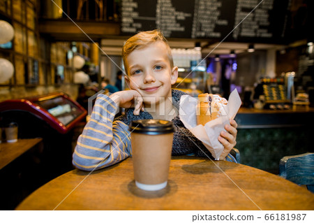 Smiling handsome little boy has breakfast in a cafe, eating fresh french croissant and drinking hot tea or chocolate Smiling handsome little boy has breakfast in a cafe, eating fresh french croissant and drinking hot tea or chocolate 66181987