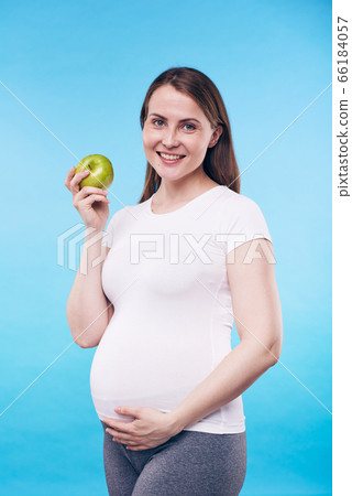 Happy pregnant female with granny smith apple touching bottom of her belly Happy pregnant female with granny smith apple touching bottom of her belly 66184057