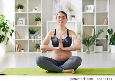 Young serene future mother keeping balance while sitting on mat in pose of lotus 66184134