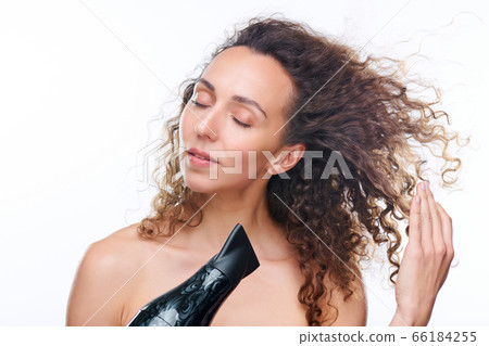 Pretty young woman with hair dryer drying her luxurious brown wavy clean hair 66184255