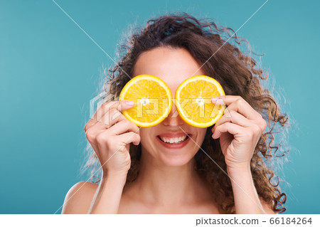 Young joyful female with two slices of fresh juicy orange by her eyes 66184264