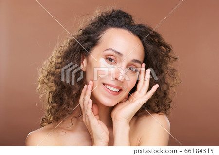Young smiling woman with curly dark hair and moisturizing patches under eyes 66184315