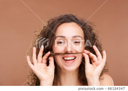 Joyful woman with toothy smile holding bunch of hair between her mouth and nose Joyful woman with toothy smile holding bunch of hair between her mouth and nose 66184347