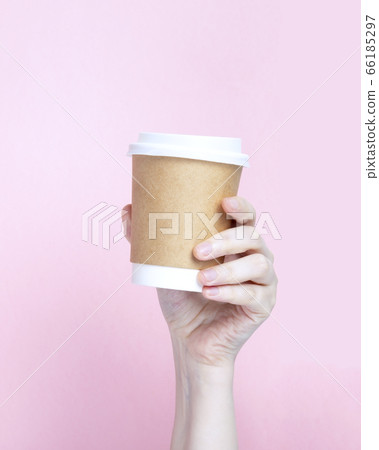 Woman's hand holds paper cup with coffee on pink 66185297