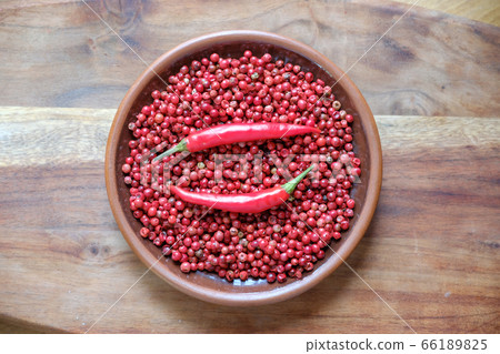 Pink peppercorns and red hot chili peppers in a clay plate standing on a wooden background. Pink peppercorns and red hot chili peppers in a clay plate standing on a wooden background. 66189825