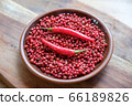 Pink peppercorns and red hot chili peppers in a clay plate standing on a wooden background. 66189826
