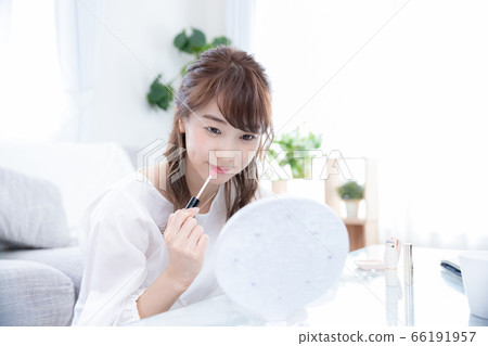 Young woman applying lip broth while looking in the mirror 66191957