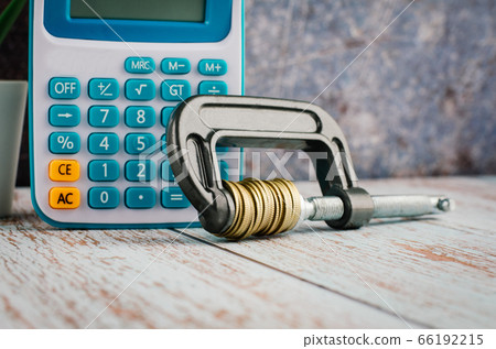 calculator and stacking coin squeezing in a G-clamp on wooden desk calculator and stacking coin squeezing in a G-clamp on wooden desk 66192215