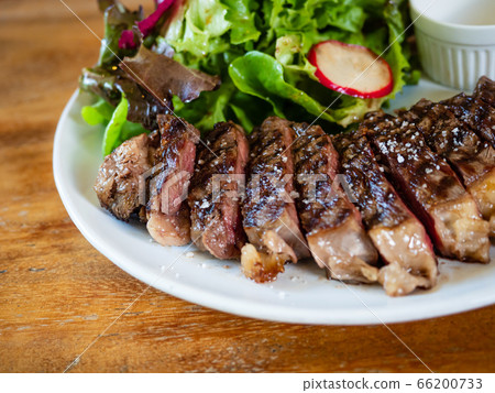 Medium Rare Steak cooked with grilled fire sauce. Sliced in a bite-size, juicy, beautiful color, appetizing, sprinkled with natural salt Decorate with salad greens on a white plate on a wooden table. Medium Rare Steak cooked with grilled fire sauce. Sliced in a bite-size, juicy, beautiful color, appetizing, sprinkled with natural salt Decorate with salad greens on a white plate on a wooden table. 66200733