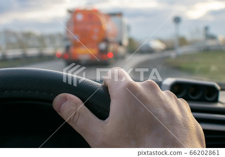 view of the driver hand at the wheel of a car against the background of a fuel tanker driving in front on the road 66202861