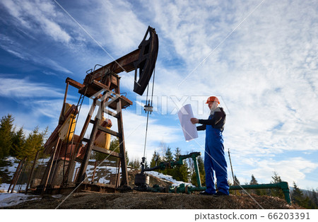 Oil worker standing by oil well pump jack. Oil worker standing by oil well pump jack. 66203391