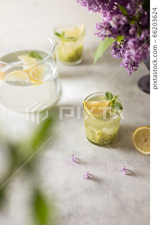 Fresh summer lemonnad with mint and kiwi stands on the table. Nearby is a bouquet of lilacs in a purple vase. 66203624