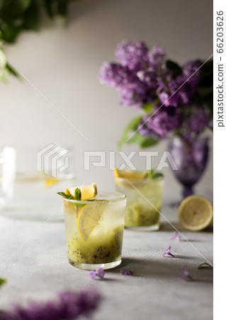 Fresh summer lemonnad with mint and kiwi stands on the table. Nearby is a bouquet of lilacs in a purple vase. Fresh summer lemonnad with mint and kiwi stands on the table. Nearby is a bouquet of lilacs in a purple vase. 66203626