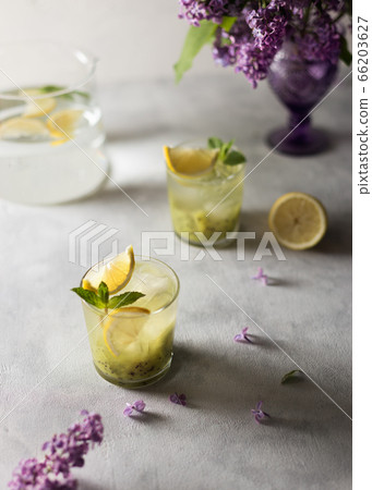 Fresh summer lemonnad with mint and kiwi stands on the table. Nearby is a bouquet of lilacs in a purple vase. 66203627