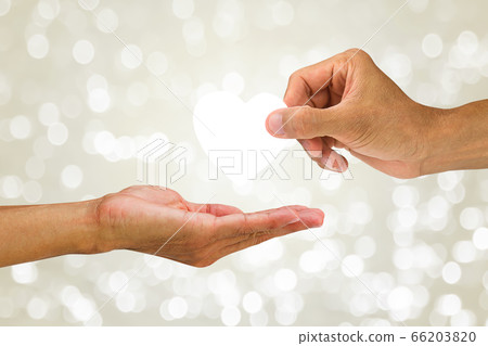 Hand giving white heart to another hand on blurred white glittering bokeh background 66203820