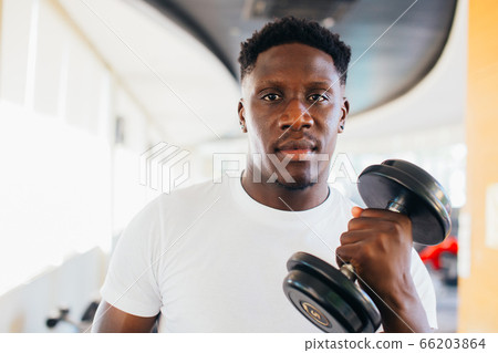 Young African American man standing and lifting a dumbbell with the rack at gym Young African American man standing and lifting a dumbbell with the rack at gym 66203864