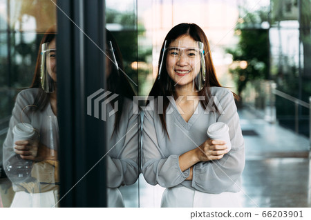 Young 20s Asian beautiful girl wearing a protective face shield and mask. Professional business woman holding a cup of coffee - Corona Virus prevention concept Young 20s Asian beautiful girl wearing a protective face shield and mask. Professional business woman holding a cup of coffee - Corona Virus prevention concept 66203901