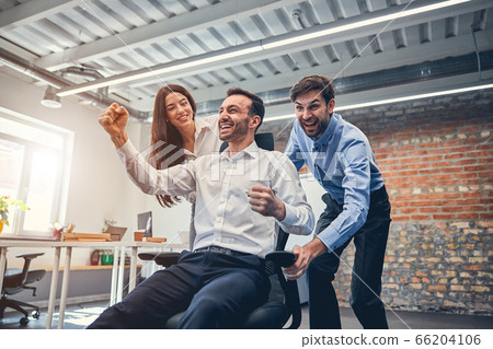 Happy co-workers racing on chairs in modern office 66204106
