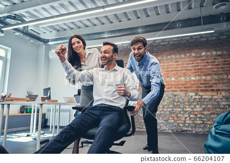 Excited managers riding on chairs in modern office 66204107