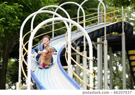 Girl playing on a slide with a bear rag Girl playing on a slide with a bear rag 66207837