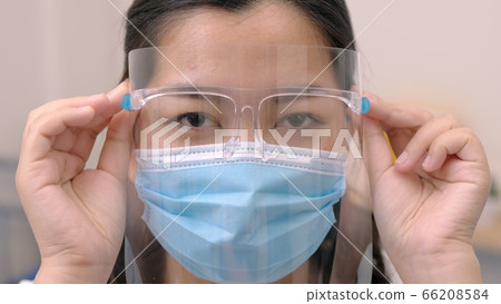 Portrait of an Asia young female who is wearing a face shield with mask rounded around her face from a frontal perspective to protect her glasses and eyes prepare to new normal. Coronavirus pandemic. Portrait of an Asia young female who is wearing a face shield with mask rounded around her face from a frontal perspective to protect her glasses and eyes prepare to new normal. Coronavirus pandemic. 66208584