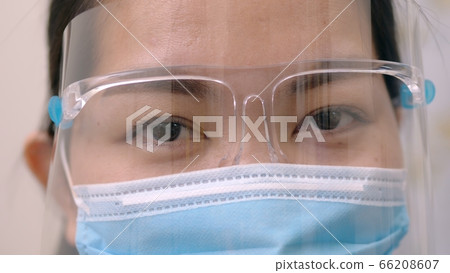 Portrait of an Asia young female who is wearing a face shield with mask rounded around her face from a frontal perspective to protect her glasses and eyes prepare to new normal. Coronavirus pandemic. Portrait of an Asia young female who is wearing a face shield with mask rounded around her face from a frontal perspective to protect her glasses and eyes prepare to new normal. Coronavirus pandemic. 66208607