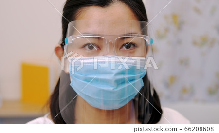 Portrait of an Asia young female who is wearing a face shield with mask rounded around her face from a frontal perspective to protect her glasses and eyes prepare to new normal. Coronavirus pandemic. Portrait of an Asia young female who is wearing a face shield with mask rounded around her face from a frontal perspective to protect her glasses and eyes prepare to new normal. Coronavirus pandemic. 66208608