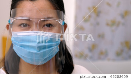 Portrait of an Asia young female who is wearing a face shield with mask rounded around her face from a frontal perspective to protect her glasses and eyes prepare to new normal. Coronavirus pandemic. Portrait of an Asia young female who is wearing a face shield with mask rounded around her face from a frontal perspective to protect her glasses and eyes prepare to new normal. Coronavirus pandemic. 66208609