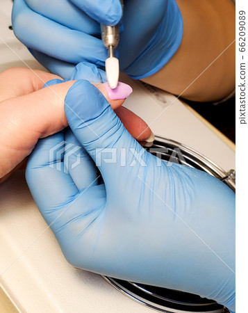 manicurist uses an electric nail file drill for manicure on women's fingers 66209089