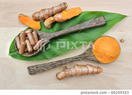 Turmeric powder; Turmeric capsules in a wooden spoon on the leaves and wooden. Turmeric root is herb for good health.Vitamin C for protect virus. Turmeric powder; Turmeric capsules in a wooden spoon on the leaves and wooden. Turmeric root is herb for good health.Vitamin C for protect virus. 66209383