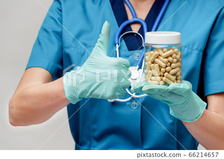 medical doctor nurse woman wearing protective mask and rubber or latex gloves - holding pills medical doctor nurse woman wearing protective mask and rubber or latex gloves - holding pills 66214657
