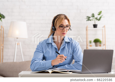 Self education at home. Concentrated woman in headphones writes in notebook and looks at laptop 66220586